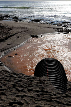 Drainpipe with dirty water on shoreline seascape.の写真素材