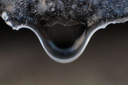 Cold clear rain drop with ice reflection inside. Handing down water drop from ice top. Macro...