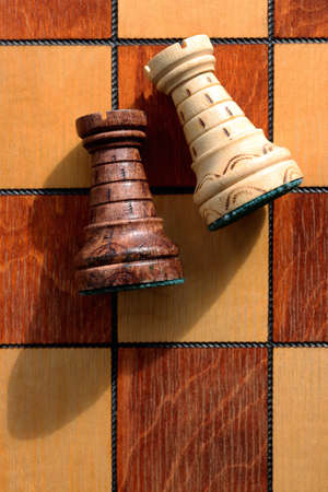 Two rooks lie on a chessboard. Wood game chessboard background.