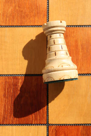 The figure of a white rook lies on a chess board. Wood game chess board background.