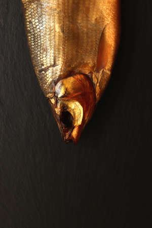 Stick out smoked fish head on black stone background.