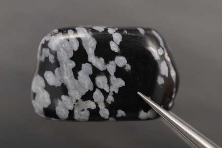 Snowflake jewel stone texture in fingers on black background. Macro closeup.