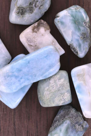 Larimar jewel heap on brown varnished wood half background. Pile mineral pebbles texture. Place for...
