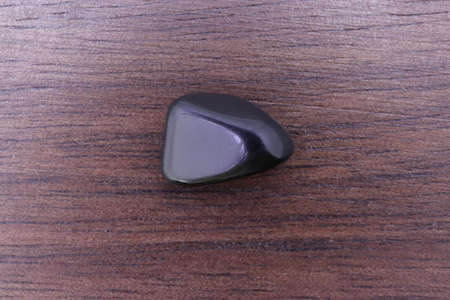 Black tourmaline jewel stone texture on light varnished wood background. Macro closeup.の写真素材