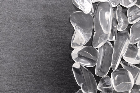 Clear quartz jewel heap on black stone half background. Pile mineral pebbles texture. Place for text.の写真素材