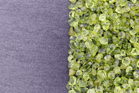 Olivine jewel texture in tweezers on light surface background. Macro closeup.