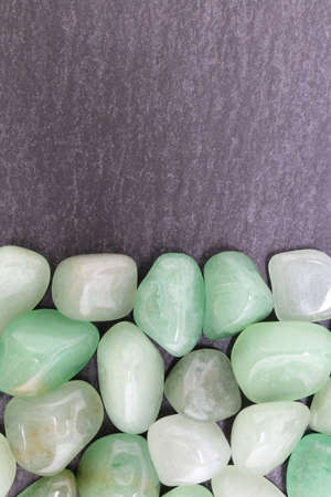 Green Aventurine rare jewel on brown varnished wood texture. Sparse mineral pebbles background.