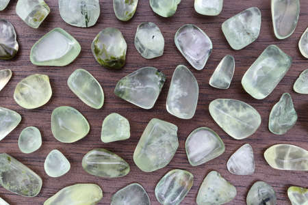 Prehnite rare jewel on half brown varnished wood texture. Sparse mineral pebbles background. Place for text.の写真素材