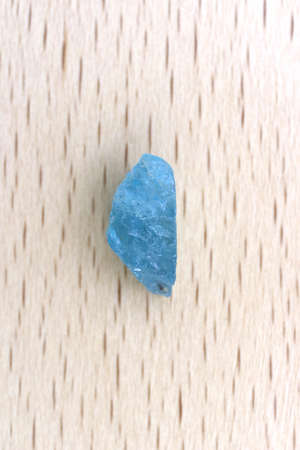 Apatite jewel stone texture on light varnished wood background. Macro closeup.