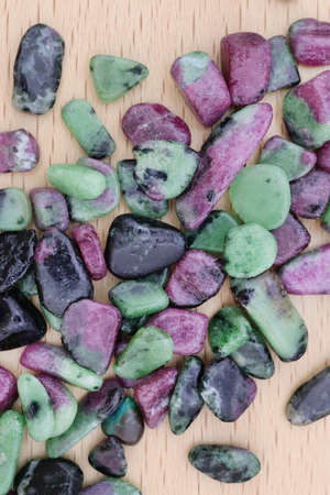 Ruby zoisite rare jewel stones texture on light varnished wood background.