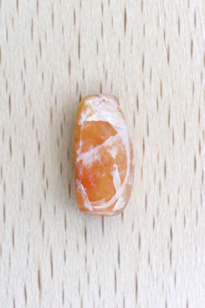 Red silk jade jewel stone texture on brown varnished wood background. Macro closeup.