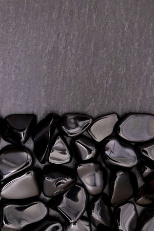 Obsidian heap jewel stones texture on half black background. Place for text.