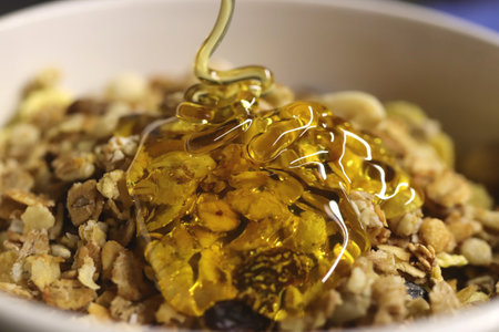 Juicy honey pours on muesli. Delicious healthy breakfast. macro closeup.