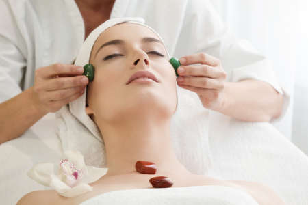 Spa salon: Young Beautiful Woman Having Chakra Facial Massage with Stones .の写真素材