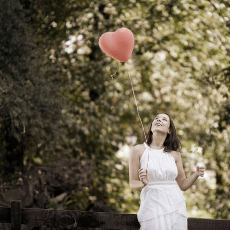 Happy Smiling Young Woman Standing with a Red Shaped Heart Balloon Outdoorsの写真素材