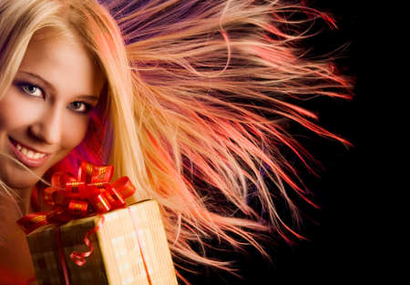Portrait of attractive smiling young woman with present in the red disco lights at the black background. Hair is scatteredの写真素材