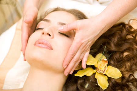 Healthy spa: young beautiful relaxing woman having a facial massage, with orchid in long brown hairの写真素材