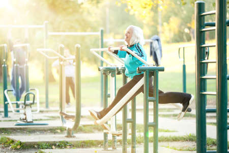 70 years old Senior Woman doing Exercises for Legs Outdoors in the Bright Autumn Eveningの写真素材
