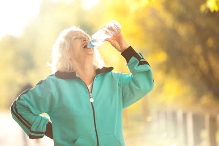 Senior Woman Drinking Water after Jogging Outdoors in the Bright Autumn Eveningの写真素材