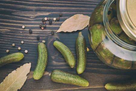 Preserved of Cucumbers: a Still Life of Dried Colorful Pepper (Black, Red, and Green), Bay Leaf, Green Cucumbers and Jars with Vinegar on the Wooden Tableの写真素材