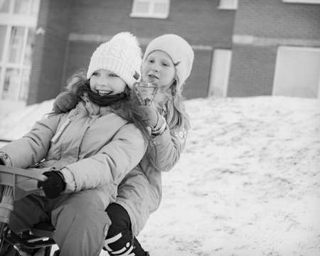 two young girls sledding together and smileのeditorial素材