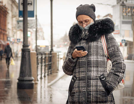 26th of October 2020, Russia, Tomsk, woman with smartphote and facemask on streetのeditorial素材