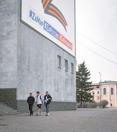 28th of April 2022, Russia, Tomsk, passerbys on street under billboard with Z letter on building