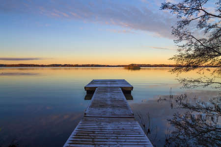 Scandinavian lake in the sunset with frozen  jetty and a tree silhouetteの写真素材