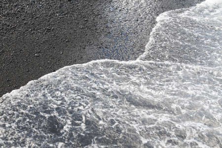 Wave breaking to the black sand beach in Maui, Hawaiiの写真素材