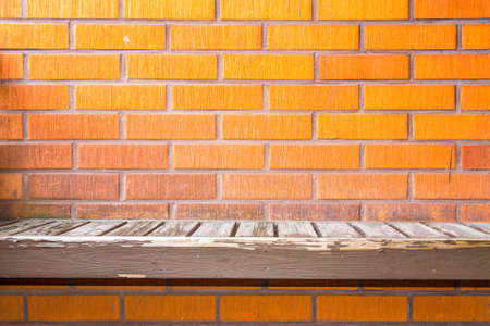 Old worn wooden seat attached to a red brick wall backgroundの写真素材