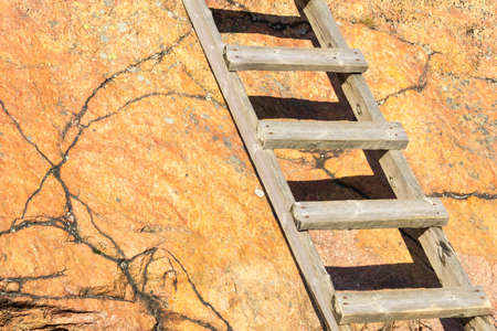 Old wooden ladder going up a red rock in sunlightの写真素材