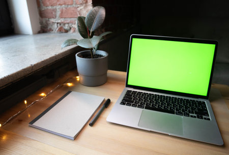 Laptop with green screen, notebook and pen on wooden table.の写真素材
