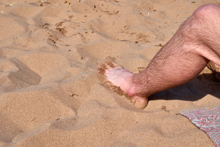 A person is comfortably laying on the warm beach with their bare feet buried deep in the soft golden sand beneath themの写真素材