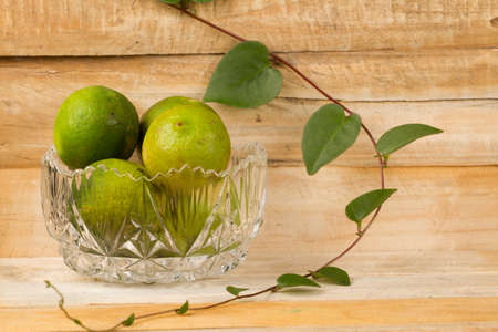 lemons in glass bowl and green plant on wood.