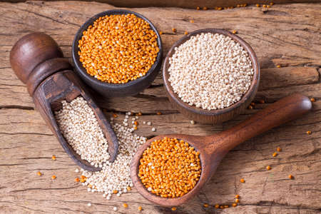 Quinoa seeds and red millet in bowl on rustic wood