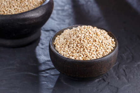Quinoa grains with spoon and bowl on black backgroundの写真素材