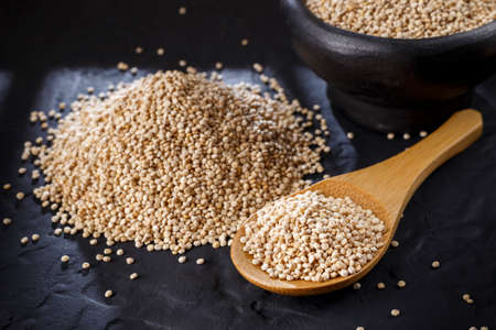 Quinoa grains with spoon and bowl on black backgroundの写真素材
