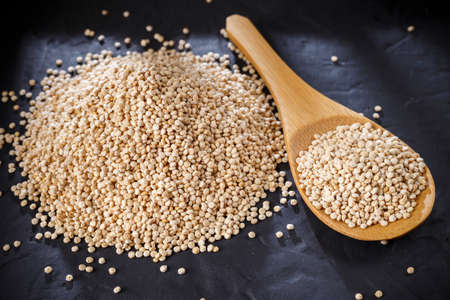 Quinoa grains with spoon and bowl on black backgroundの写真素材