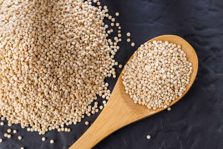 Quinoa grains with spoon and bowl on black background