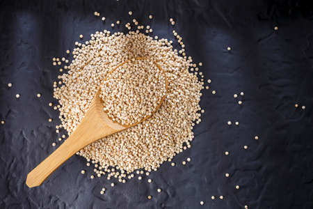 Quinoa grains with spoon and bowl on black backgroundの写真素材