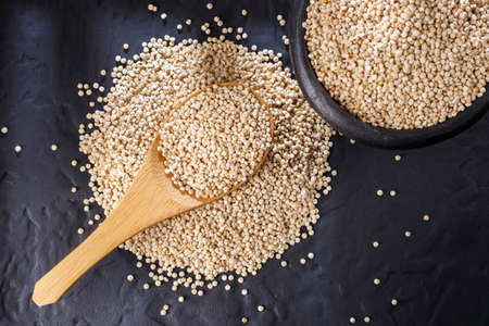 Quinoa grains with spoon and bowl on black backgroundの写真素材
