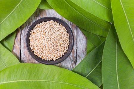 bowl with quinoa grains surrounded by green leaves on wooden background, top viewの写真素材