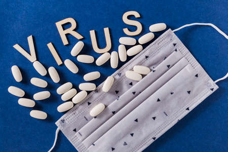 Virus word with wooden letters, compressed medicine tablets and face protection mask, on blue...