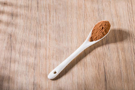 spoon with cocoa powder on wooden table, space for text, top view