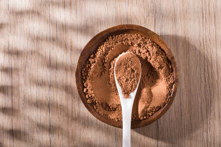 spoon with cocoa powder on wooden table, space for text, top view