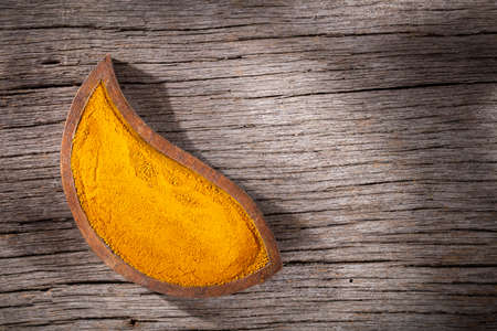 Turmeric powder in bowl on wooden background (Curcuma longa)