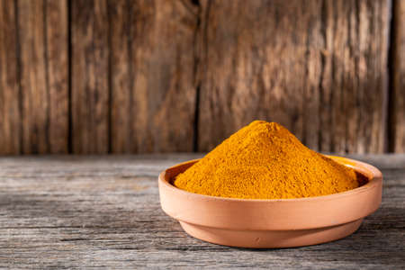 Turmeric powder in bowl on wooden background (Curcuma longa)