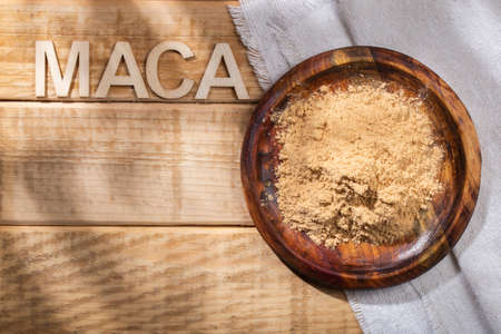 Maca powder, in wooden bowl on the table, nutritional substance from Peru.