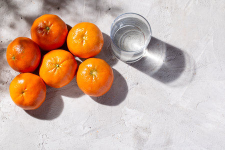pile of fresh tangerines and glass with water on the concrete table, top viewの写真素材