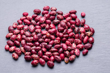 A closeup image of red kidney beans scattered on a slate surface, showing their mottled red and white coloration.の写真素材